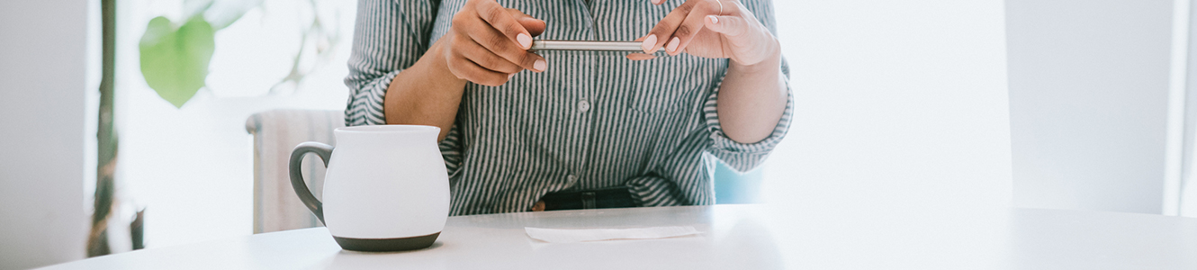 Woman at kitchen table that is taking a picture of a check to deposit it to her banking account. 